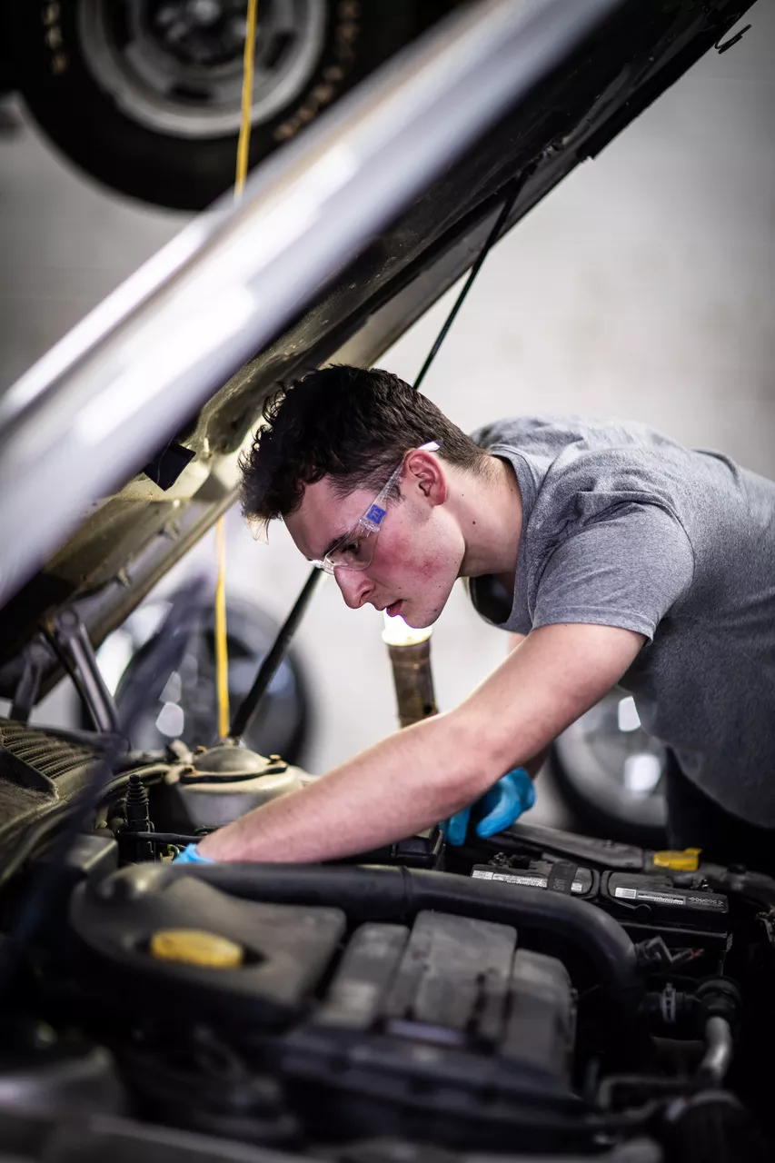 Male student wearing safety glasses working under the hood of an automobile
