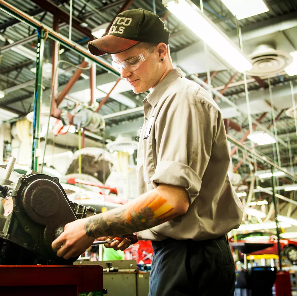 Student in baseball cap working on a part in automotive shop